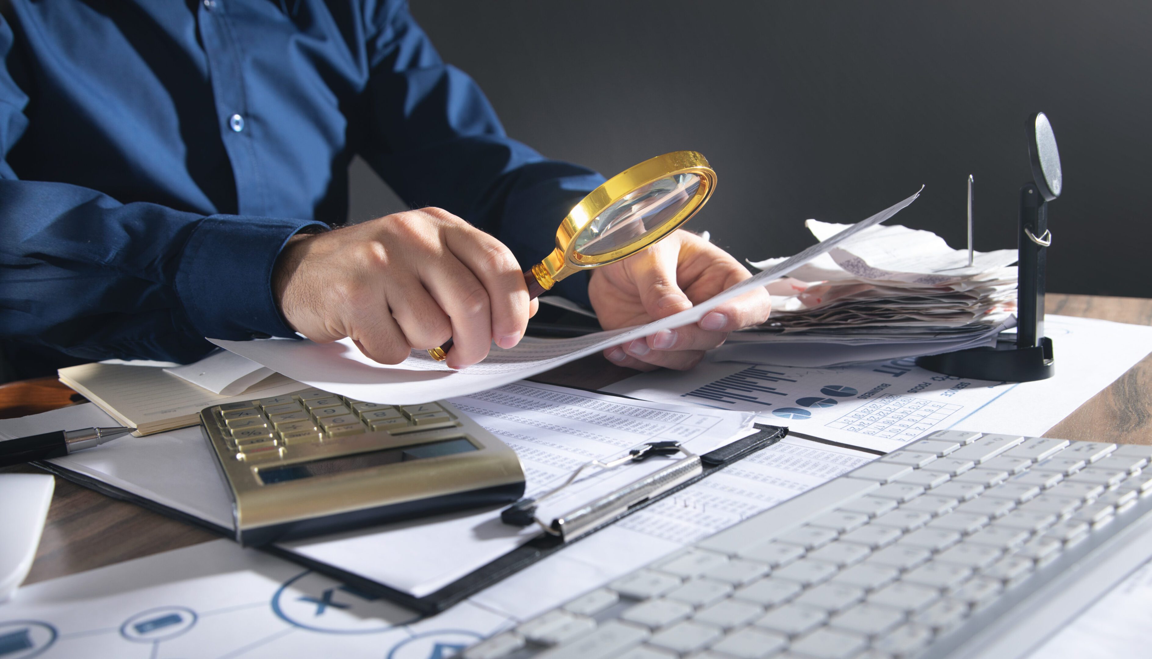 Businessman holding magnifying glass with documents.